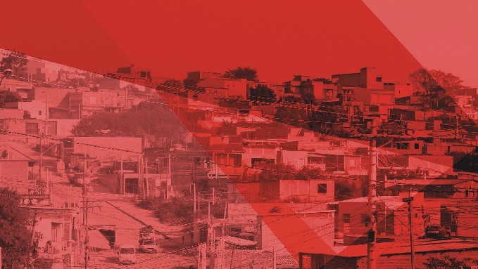 Imagem mostra panorâmica de casas, muitas delas com paredes de tijolos, e postes e fios elétricos no primeiro plano. A imagem foi tratada e tem tons avermelhados.