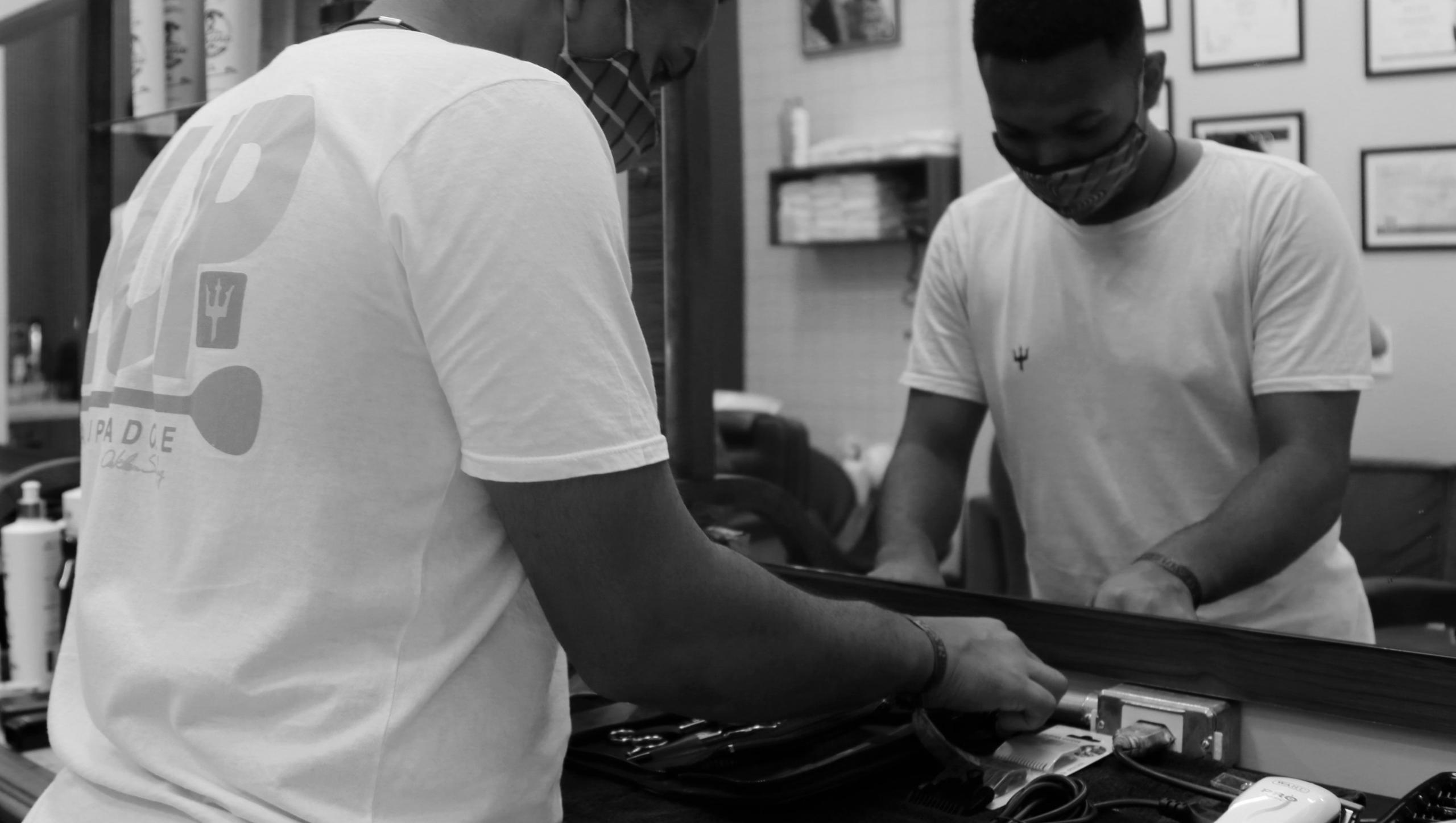 Jovem está dentro de um salão de cabelereiro com diversos instrumentos de trabalho, como tesoura, máquina e secador de cabelo