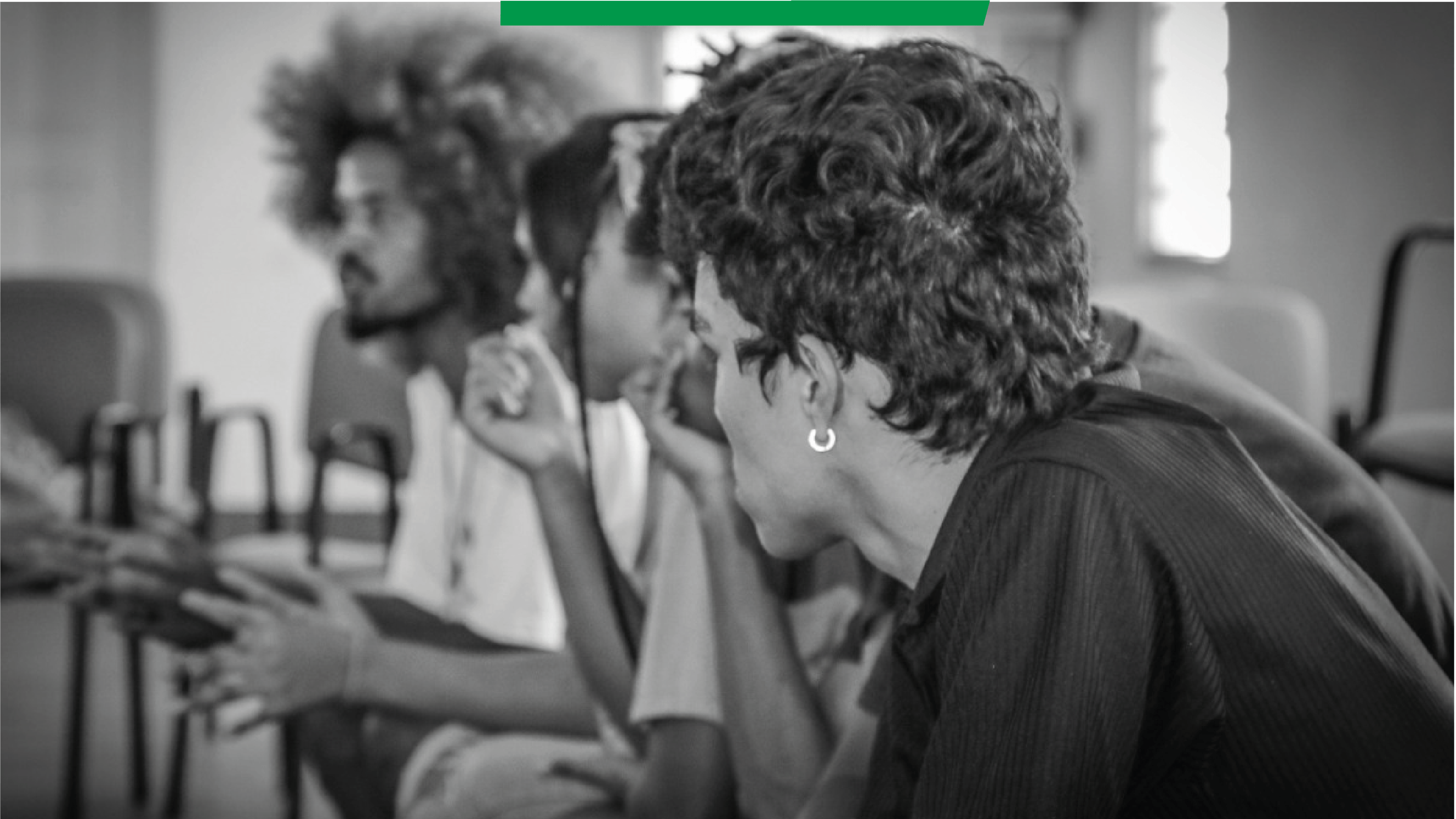 Foto em preto e branco mostra uma fileira de jovens sentados, que olham atentamente para a lateral, como se estivessem ouvindo alguém.